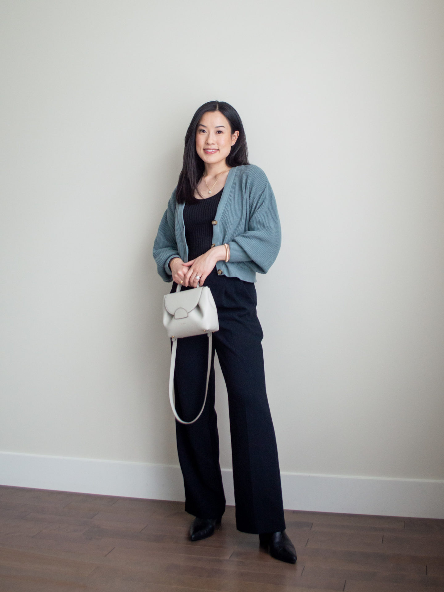 Sharon of Her Simple Sole is showcasing an outfit from a weekend trip in a backpack featuring a black ribbed tank top, a cropped cardigan, black wide leg pants, black pointed toe ankle boots, and an off-white crossbody bag | minimalist outfits | fall outfit ideas | simple outfit ideas